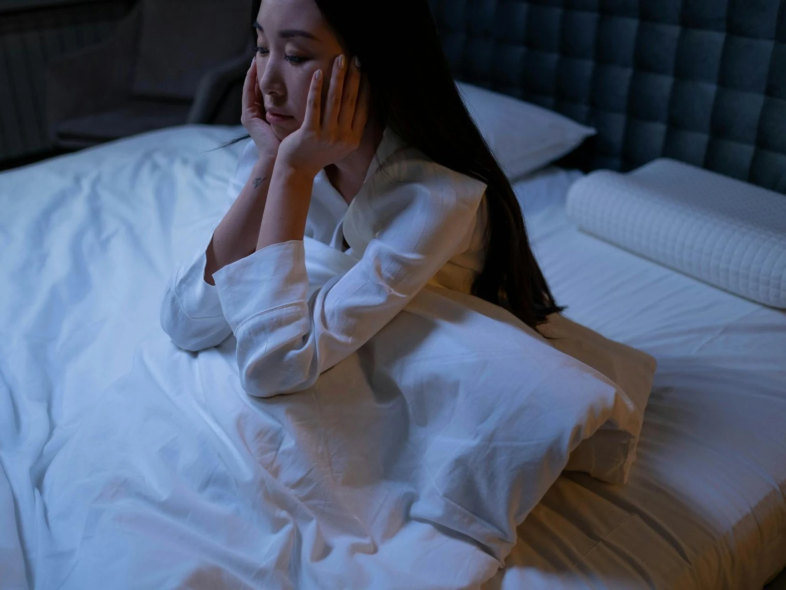 在漆黑卧室的床上坐着、双手托腮清醒着的女性，无法入睡的深夜失眠场景
